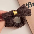 Detail eines flauschigen braunen Haargummis mit einer goldenen Smiley-Metallschnalle - Smiley Dunkelkaffee Haargummi