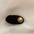 Detail einer eleganten schwarzen Lammwoll-Haarklammer mit mattgoldenem Metallknopf - Oval / Schwarz
