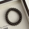 Macro shot of a high-elastic black spiral hair tie on a minimalist wooden tray - Spiral Telephone Wire Style / Brown