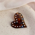 Dettaglio del fermaglio per capelli in acetato a cuore con perle su piatto beige - Blu Caffè