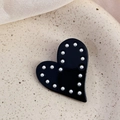 Dettaglio del fermaglio a cuore in acetato con bordo di perle su sfondo in ceramica - Nero