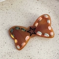 Dettaglio macro della molletta a fiocco marrone con cuciture colorate e un motivo a stella - Fiocco Cucito Caffè