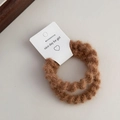Dettaglio di due elastici per capelli marroni in peluche con texture soffice su sfondo beige - Albicocca