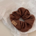 Close-up of a brown ribbed knit scrunchie with a leather handmade smiley face tag - Light Coffee