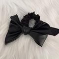 Detail eines schwarzen Leder-Haargummis mit großer Schleife auf weißem Plüschhintergrund - Plissierter Lederbogen-Stil / Schwarz