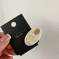 Detail of oval acetate hair clip with POKO FOSCA metal logo plate on cream marble resin - Cream