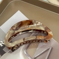 Detail of tortoiseshell acetate claw clip with golden logo and crescent hollow design - Amber