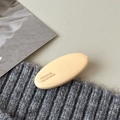 Macro detail of beige oval hair clip with France Handmade text on a knit background - Apricot