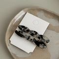 Close-up of twisted marble acetate hair clips with golden metal base on a ceramic tray - Transparent Black