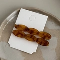 Dettaglio di due fermagli per capelli in resina tartarugata ambrata su supporto - Caffè Caramello