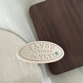 Detail van een crèmekleurige ovale haarklem met SAVON-reliëf en turquoise zirkoonaccent - Crèmewit