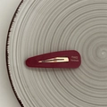 Dettaglio di fermaglio per capelli rosso scuro con scritta dorata su vassoio ceramico - Borgogna