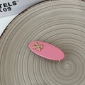Detail of pink oval hair clip with gold bow embellishment on textured ceramic plate - Pink
