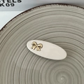 Detail of elegant creamy white oval hair clip with a gold bow on textured ceramic plate - Off-white