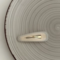 Dettaglio di un fermaglio per capelli a triangolo crema su un piatto di ceramica decorato - Bianco Trasparente