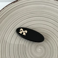 Detail of a chic black oval hair clip with a delicate gold bow on a ceramic plate - Black
