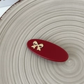 Close-up of a red oval resin hair clip featuring a delicate gold metal bow on a tray - Dark Red