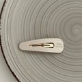 Detail of cream-colored handmade BB hair clip with gold metal base on a ceramic plate - Off-white