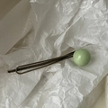 Vue détaillée de la barrette en métal bronze ornée d'une perle sphérique vert clair - vert clair