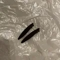 Close-up of two minimalist black glossy hair clips on a textured white background - Gun Grey Solid Ellipse