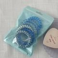 Close-up of blue gradient spiral hair ties in a frosted zipper bag on white fabric - Blue