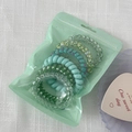 Close-up of colorful spiral phone cord hair ties set in a translucent zipper pouch - Green