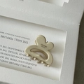 Detail shot of a cream-colored acetate hair claw with a gold label on a minimalist tray - Off White