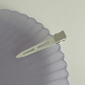 Close-up of white matte metal no-crease hair clip on a textured decorative plate - White