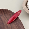 Détail d'une barrette ovale en acétate rouge avec inscription dorée sur plateau en bois - Rouge