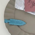 Close-up of a light blue wavy seamless hair clip on a ceramic tray with a thank you card - Blue