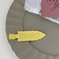 Macro view of a yellow metal duckbill hair clip with textured wavy surface and matte finish - Yellow