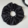 Dettaglio di un elastico in raso nero con otto perle bianche su una superficie bianca - Nero
