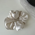 Detail view of the champagne satin fabric texture and pleated edge on the hair scrunchie - White