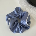 Detail of blue satin scrunchie featuring white contrast trim and smooth pleated texture - Blue