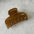 Primer plano de pinza de pelo en resina color ámbar con logotipo dorado y muelle metálico - Marrón