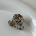 Détail d'une mini pince à cheveux en acétate AMI BEAR avec texture marbrée et lettrage doré - Texture multicolore