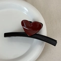 Detail view of a black shark hair claw clip with a glossy red heart ornament on a plate - Heart-shaped Color Scheme - Black