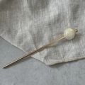 Detailweergave van elegante gouden haarpeld met een grote witte gemarmerde parelkraal - Beige