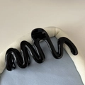 Gros plan d'une pince à cheveux noire brillante en forme de vague sur tissu bleu - Noir