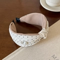 Dettaglio di un cerchietto a pois con perla e cristallo su un tavolo di legno raffinato - Beige a Pois