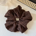 Macro-opname van een grote scrunchie met luipaardprint op witte getextureerde stof - Donkere Koffie Luipaard