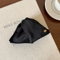 Detalle de pinza para el pelo en tela negra con textura de puntos y logo dorado de lujo - Pinza de Pelo Triangular Negro
