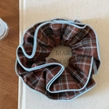 Detail of a brown plaid scrunchie with blue stitched edges on a textured background - Coffee Plaid