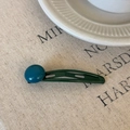 Detalle de una horquilla de metal verde oscuro con una cuenta azul sobre tela lino - Azul