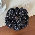 Primer plano detallado de un scrunchie floral negro con etiqueta sobre un tapete tejido - Coletero de tela