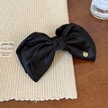 Dettaglio del fermaglio per capelli a fiocco in raso nero con emblema in oro di lusso - Molla Banana Media / Molla Banana Nera