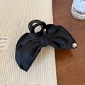 Dettaglio di un'elegante pinza per capelli con fiocco in raso nero e logo in metallo dorato - Grande Pinza per Capelli / Molla Capelli Nera