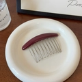 Détail d'un peigne à cheveux bordeaux à 12 dents présenté sur un plateau en céramique - Bordeaux