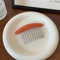 Détail d'un peigne à cheveux orange à 10 dents en métal sur une assiette en céramique - Rouge Orangé