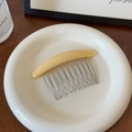 Close-up of cream yellow hair comb with twelve silver metal teeth on a white plate - Beige